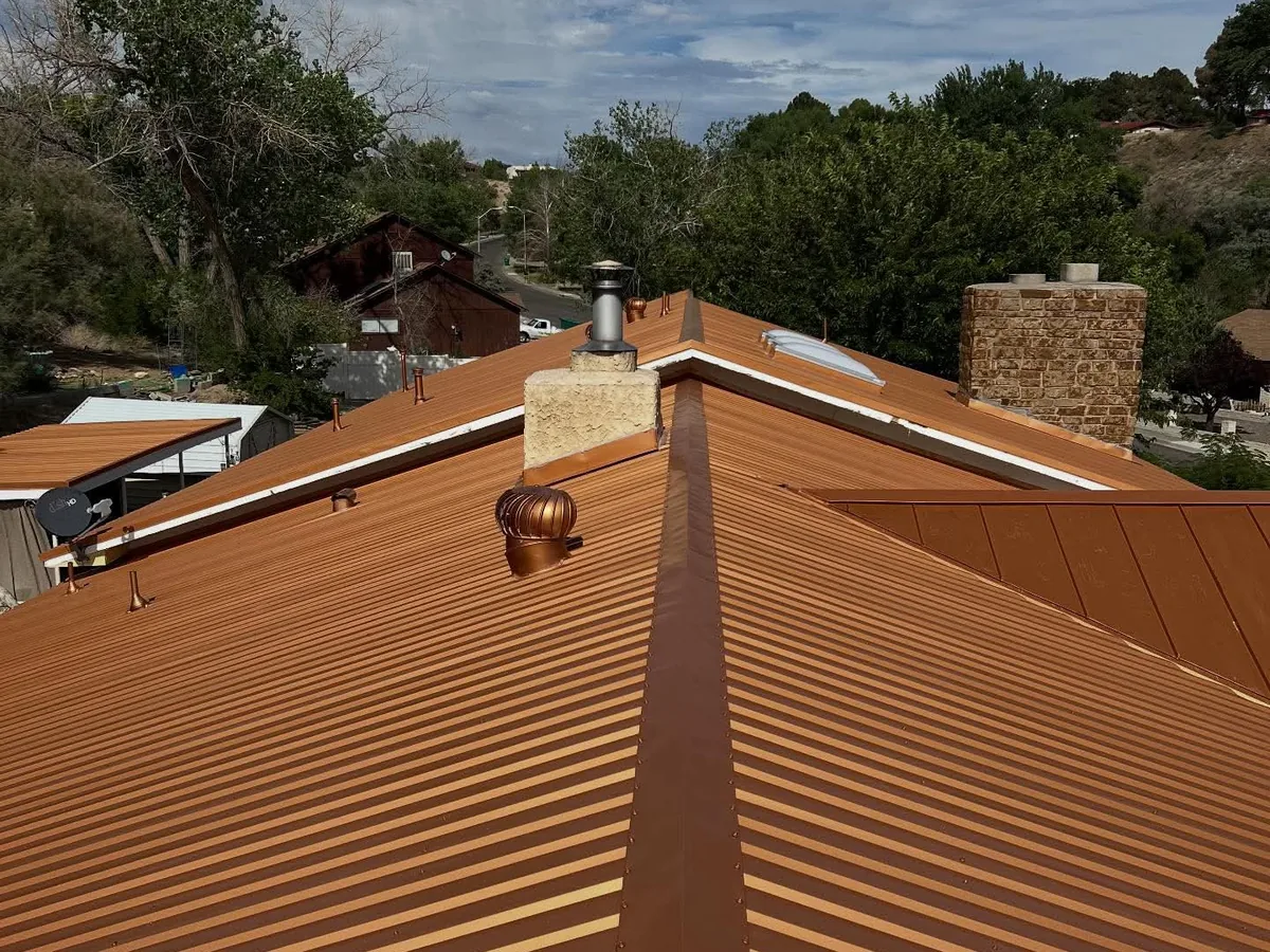 Orange metal roof panels with a turbine vent and stucco chimney